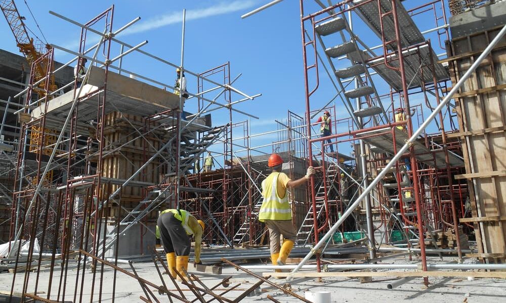 Trabalhadores da construção civil montando andaimes tubulares em uma obra, com estruturas metálicas e equipamentos de segurança no local.